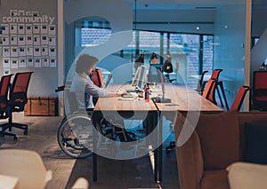 Disabled businessman in wheelchair working overtime alone at his desk in an office late at night