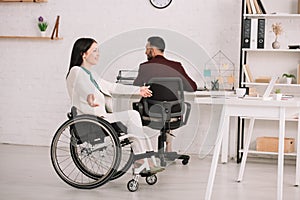 Disabled businesswoman gesturing while sitting in wheelchair near colleague