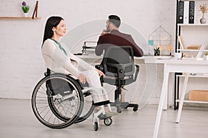 Disabled businesswoman looking away while sitting in wheelchair near colleague