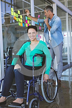 Disabled businesswoman looking at camera while male executive writing on sticky notes