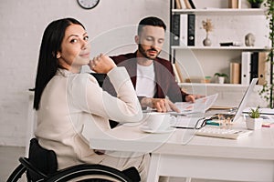 Disabled businesswoman sitting at desk in office near handsome colleague