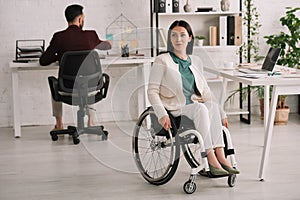 Disabled businesswoman sitting in wheelchair in office near colleague
