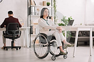 Disabled businesswoman sitting in wheelchair in office near colleague