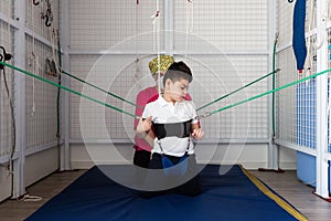 Disabled caucasian child doing physiotherapy rehabilitation on elastic cords with physiotherapist, osteopath during coronavirus.