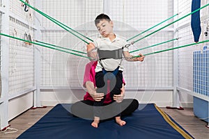 Disabled caucasian child doing physiotherapy rehabilitation on elastic cords with physiotherapist, osteopath during coronavirus.