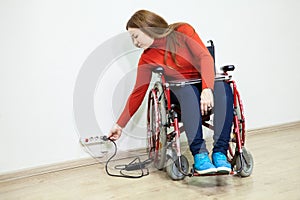 Disabled Caucasian woman in wheelchair stretching to power socket in wall for turn on laptop