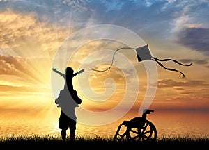 Disabled child on shoulders of dad playing with kite and wheelchair near sea sunset