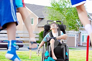 Disabled child in wheelchair watching children play at park