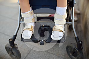 Disabled girl sitting in wheelchair. On her legs orthosis. Child cerebral palsy. Disability. Inclusion. Family with disabled kid
