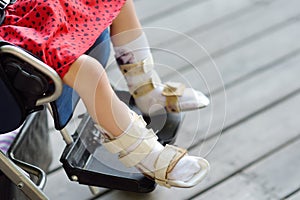 Disabled girl sitting in wheelchair. On her legs orthosis. Child cerebral palsy. Disability. Inclusion. Family with disabled kid