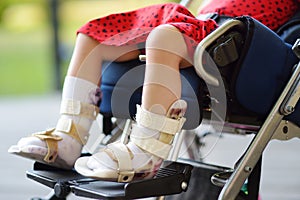 Disabled girl sitting in wheelchair. On her legs orthosis. Child cerebral palsy. Disability. Inclusion. Family with disabled kid