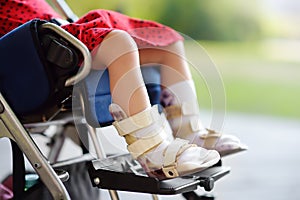 Disabled girl sitting in wheelchair. On her legs orthosis. Child cerebral palsy. Inclusion photo