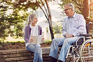 Disabled grandfather in park spending time together with his granddaughter reading book.