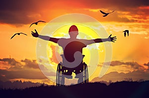 Disabled handicapped man has a hope. He is sitting on wheelchair and stretching hands at sunset photo