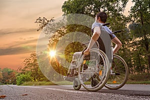 Disabled or handicapped young man on wheelchair in nature at sunset