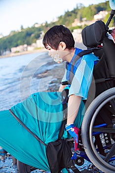 Disabled little boy in wheelchair down by water on beach