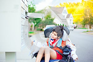 Disabled little boy in wheelchair getting mail from mailbox