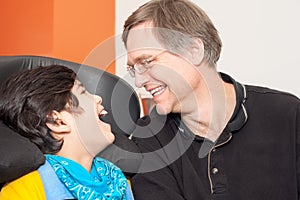 Disabled little boy in wheelchair laughing with father in hospital room