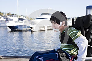 Disabled little boy in wheelchair out on pier by lake