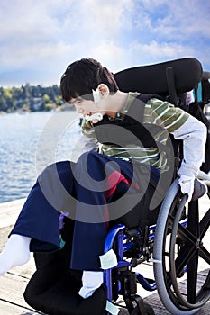 Disabled little boy in wheelchair out on pier by lake