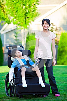 Disabled little boy in wheelchair with sister on grassy lawn out