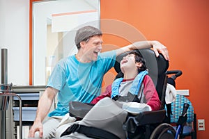 Disabled little boy in wheelchair talking with father in hospital room