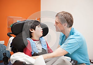 Disabled little boy in wheelchair talking with father in hospital room