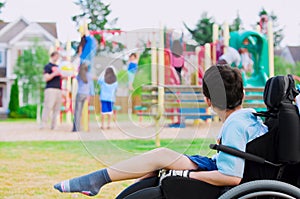 Disabled little boy in wheelchair watching children play on play