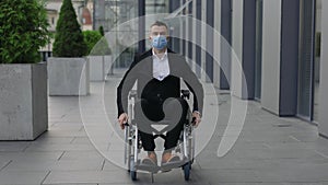 Disabled male ceo executive in 40s wearing medical protective mask and looking ahead while moving at street. Man in