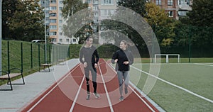 Disabled man with amputated leg and sports woman jogging. Male sportsman with running blade and female person run on