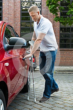 Disabled man holding crutches opening door of a car