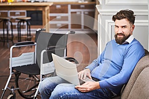 Disabled man sitting on a comfy couch and using a laptop