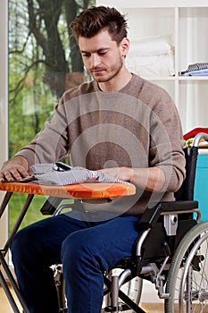 A disabled man sitting and ironing shirt