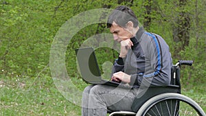 Disabled man thinks problems wheelchair with a laptop in working on green background nature