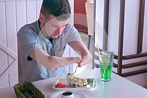 Disabled man with two amputated stump hands eats sushi rolls in cafe with fork.