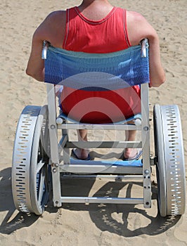 Disabled man with undershirt on the wheelchair in the sandy beac