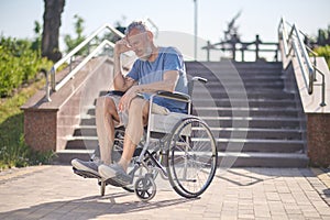 A disabled man in a wheel chair outdoors looking thoughtful