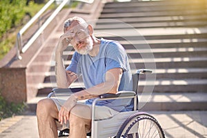 A disabled man in a wheel chair outdoors looking thoughtful