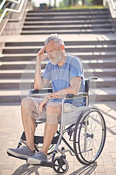 A disabled man in a wheel chair outdoors looking thoughtful