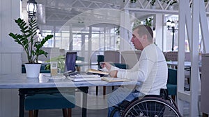 Disabled man in wheel chair talking using app on laptop computer during online education sitting at table with books and