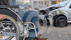 Disabled man on wheelchair had car accident. Crashed car in background.