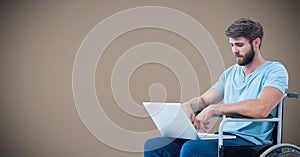 Disabled man in wheelchair on laptop with brown background