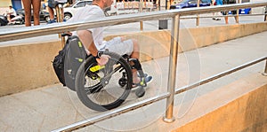 Disabled man in a wheelchair moves on a ramp to the beach.