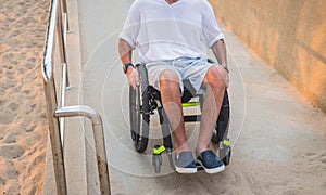 Disabled man in a wheelchair moves on a ramp to the beach.