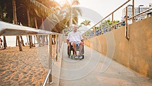 Disabled man in a wheelchair moves on a ramp to the beach.