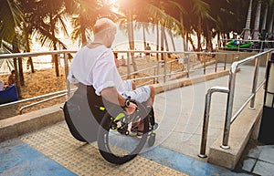 Disabled man in a wheelchair moves on a ramp to the beach.