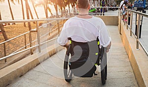 Disabled man in a wheelchair moves on a ramp to the beach.