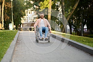 Disabled man in wheelchair rides on a path in park