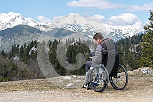 Disabled man on wheelchair using camera in nature, photographing beautiful mountains