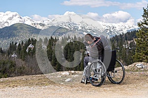 Disabled man on wheelchair using camera in nature, photographing beautiful mountains